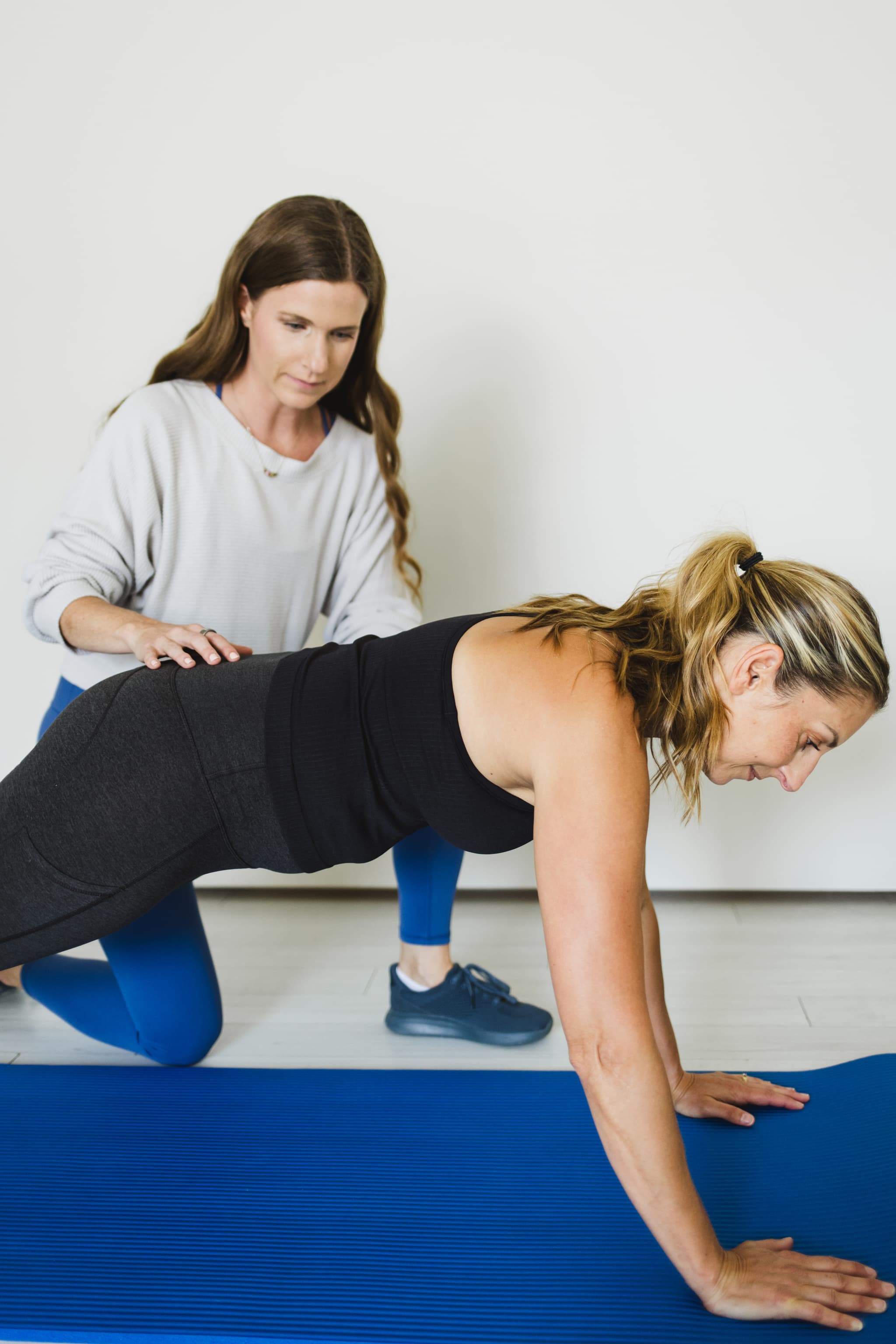 Pelvic floor physical therapist is educating a patient through plank exercise in a gym setting.