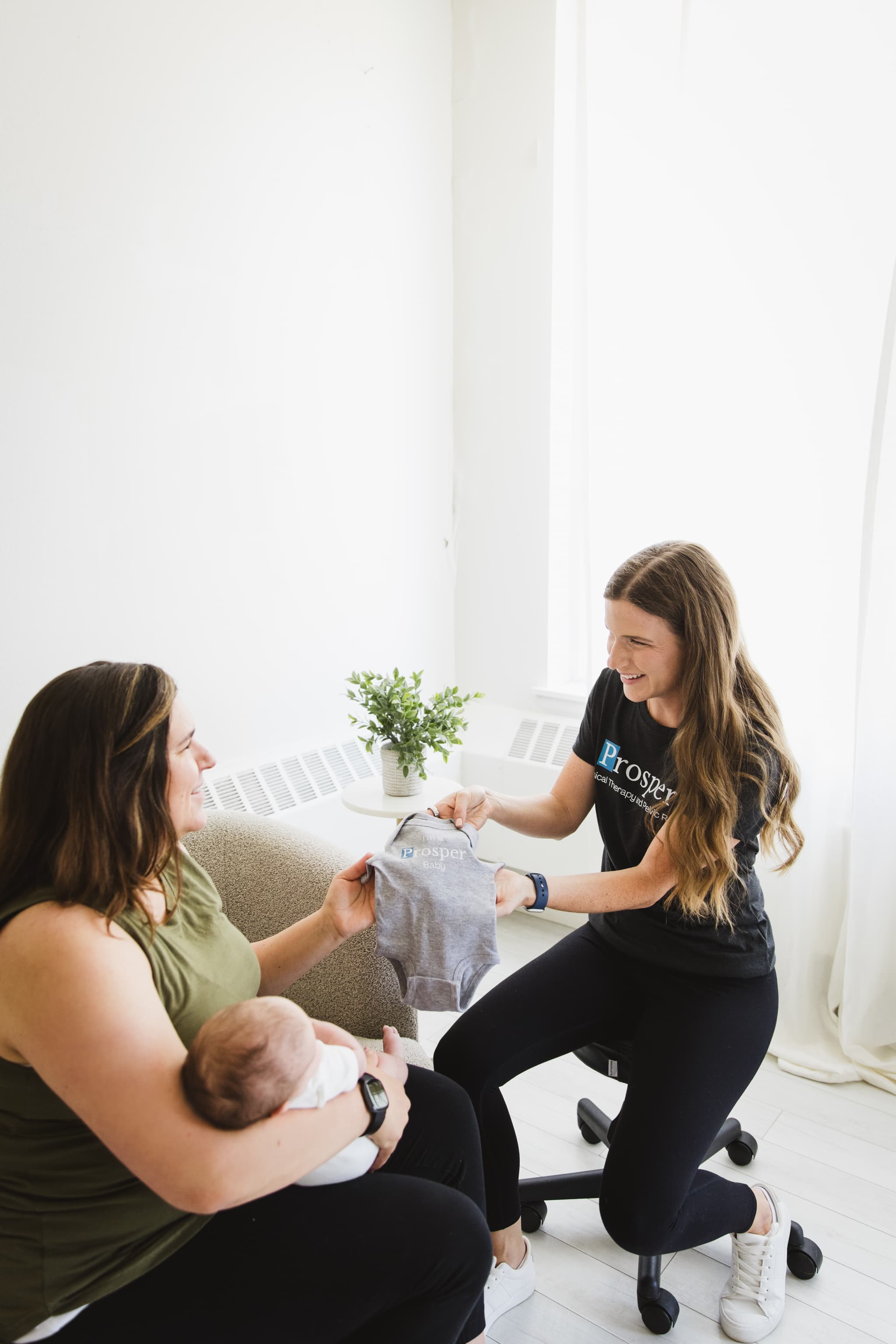 Compassionate image of pelvic floor physical therapist giving a onsie to a recently postpartum mom as a gift for her baby.
