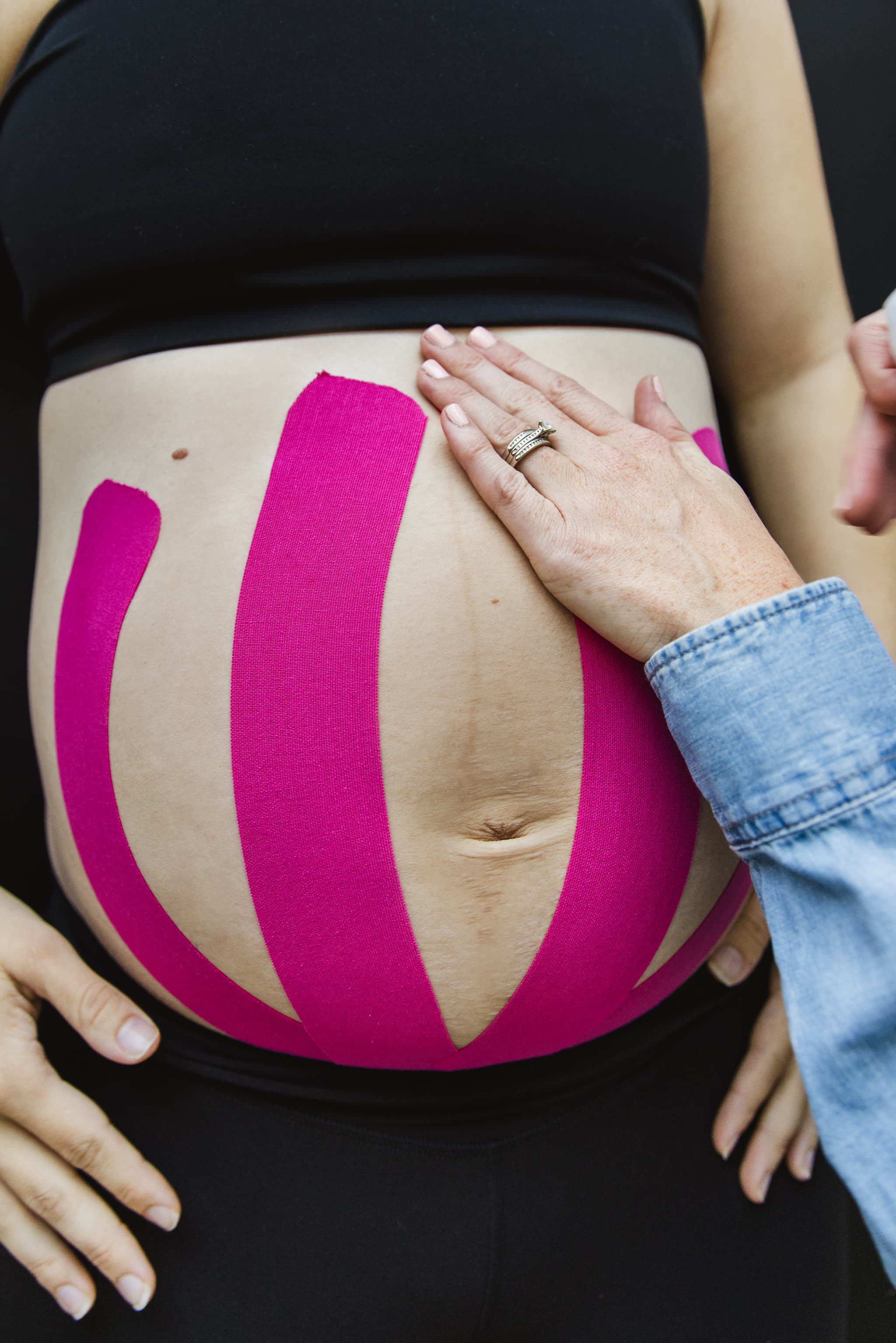 Image of pelvic floor physical therapist applying kinesio-tape to a pregnant woman's belly to provide support to her growing baby.