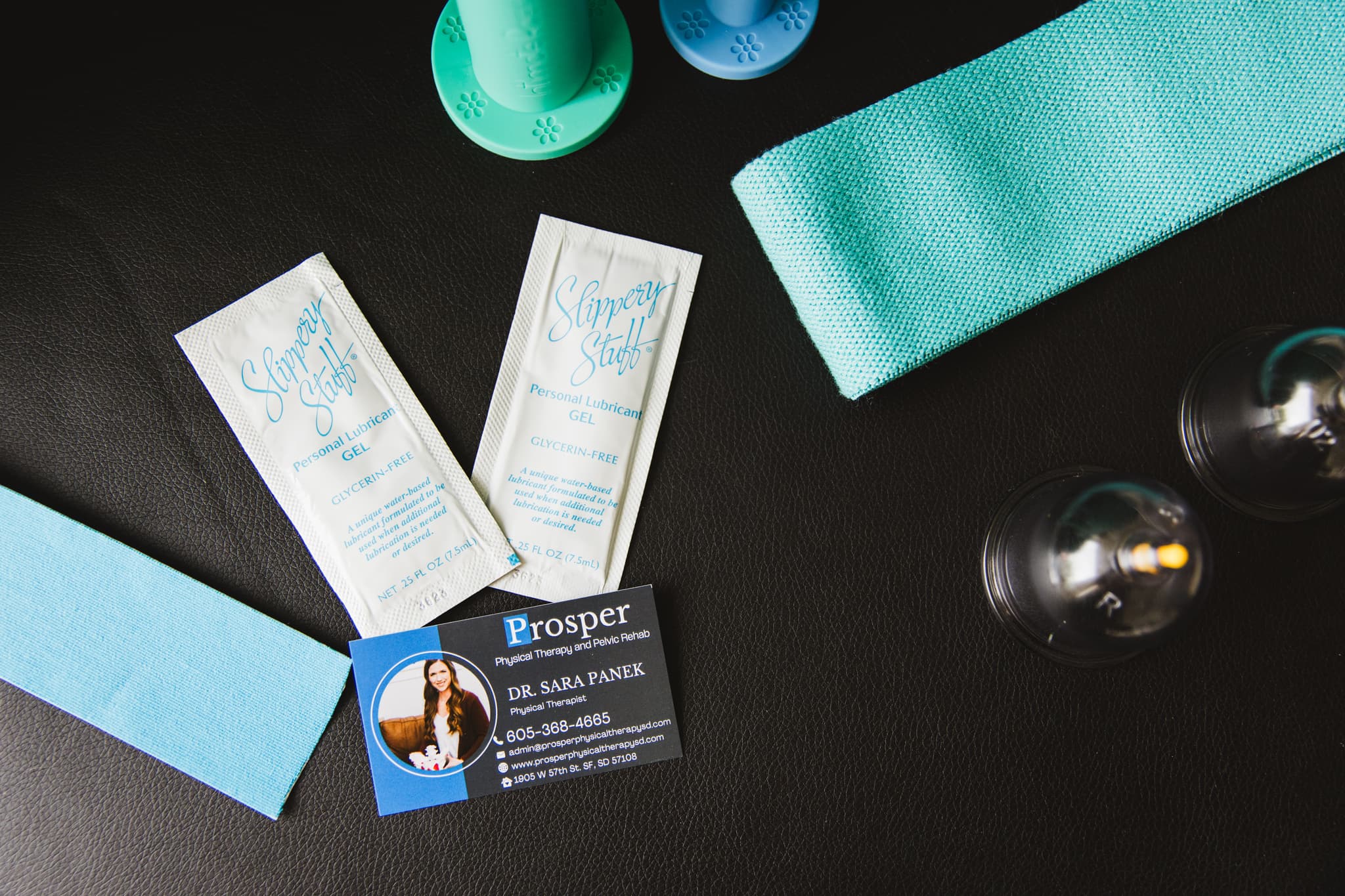 Detail image of lubrication, exercise pants, vaginal dilators, cupping tools and a business card on the therapy table.