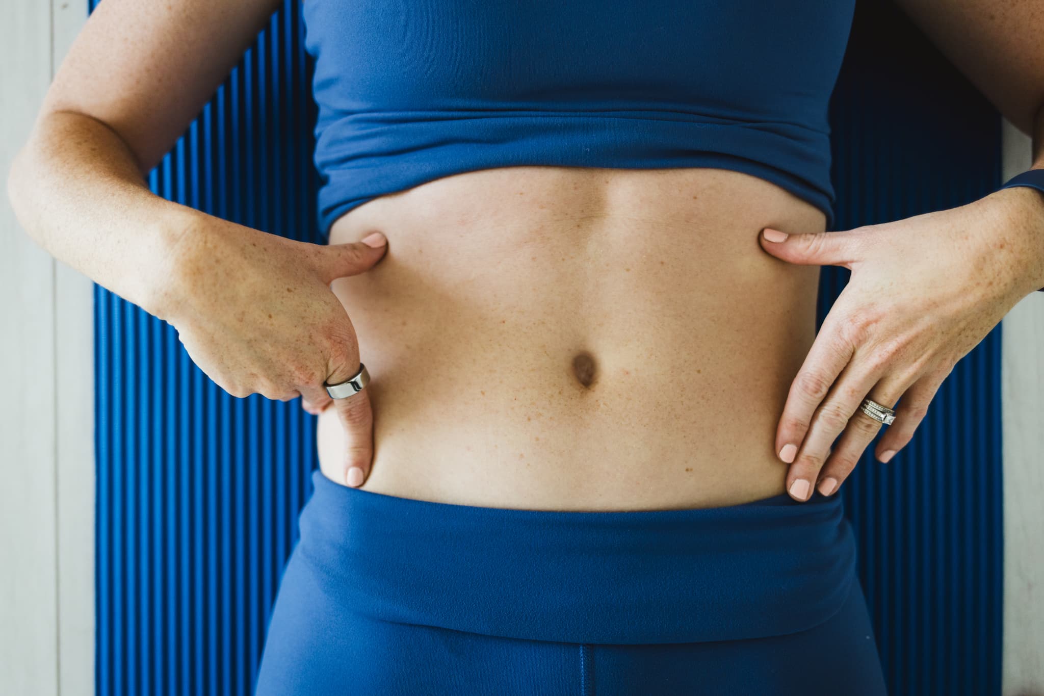 Close up image of a woman placing her fingers on the hip bone and ribcage on both sides of her body demonstrating ribcage mobility in relation to lower core activation.